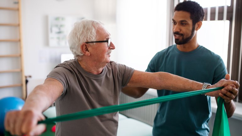 Mann in einem Rückenschmerzzentrum, der Übung mit Physiotherapeut macht.