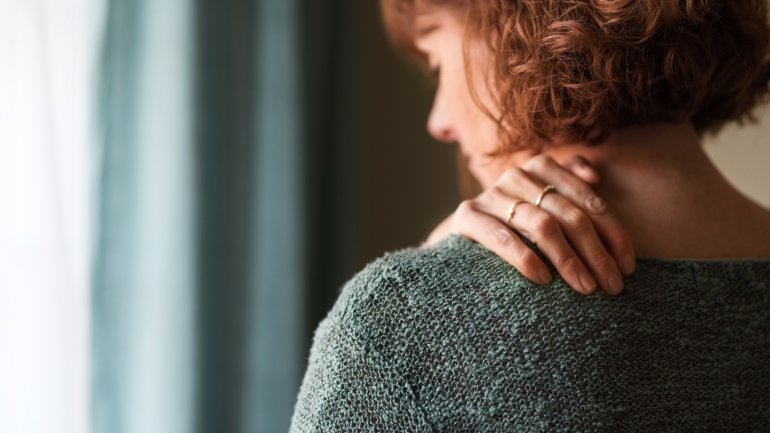 Eine Frau hält sich die Hand in den schmerzenden Nacken