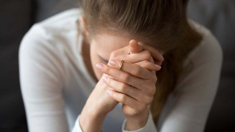 Frau sitzt verzweifelt mit den Händen vor dem Gesicht auf dem Bett