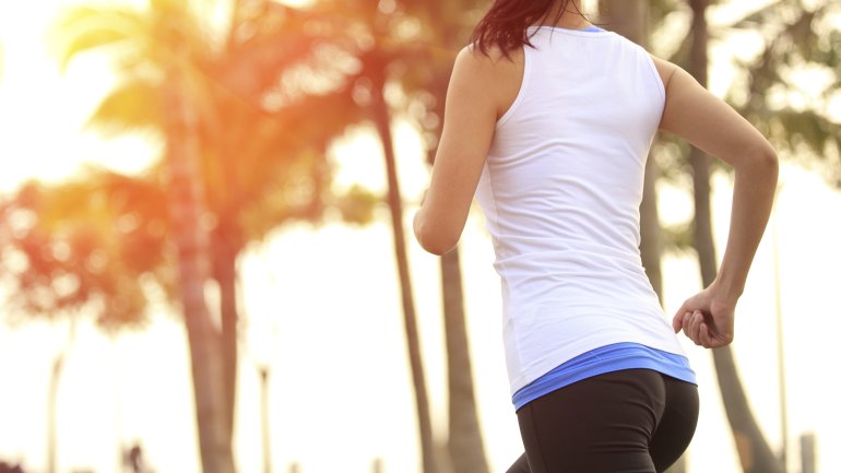 Eine Frau von hinten beim Joggen unter Palmen